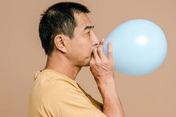 A man blowing up a blue balloon