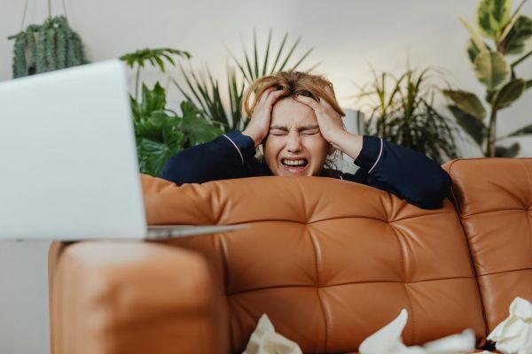 A woman leaning on a sofa and holding her head in her hands in despair