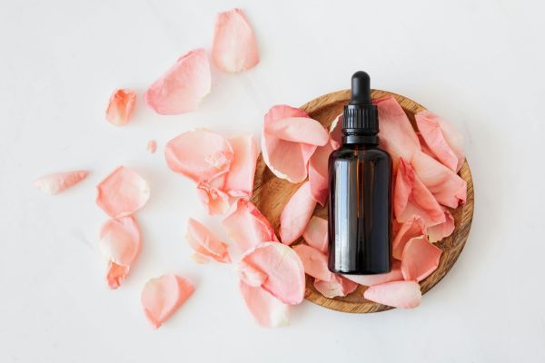 A wooden bowl with a bottle and rose petals scattered around it.