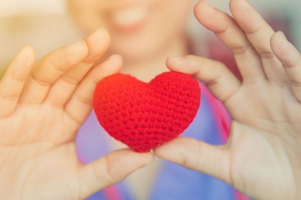 A woman holding a knitted heart between her fingers