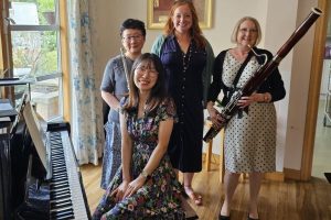 Four people with musical instruments and one person sitting at a piano.