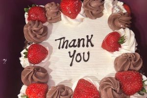 A chocolate cake with strawberries and cream with thank you written on oit.