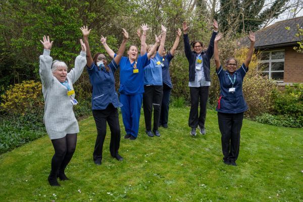 Staff on grass jumping with their hands in the air.