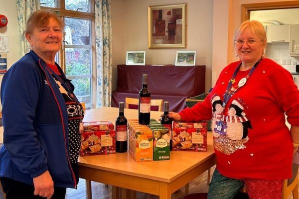 Two people in Christmas jumpers standing next to a table with food and drinks.