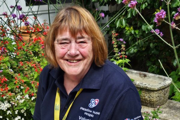 Carol standing in front of colourful flowers and plants.