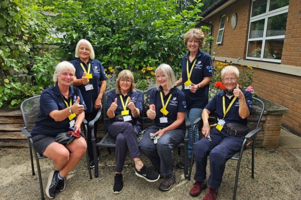 Volunteers sitting in a garden with their thumbs up.