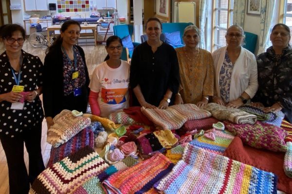 The knitting group in front of a table full of knitted blankets, hearts and muffs.