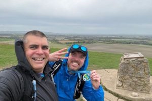 Derek and a friend holding up their medals on the top of a mountain.