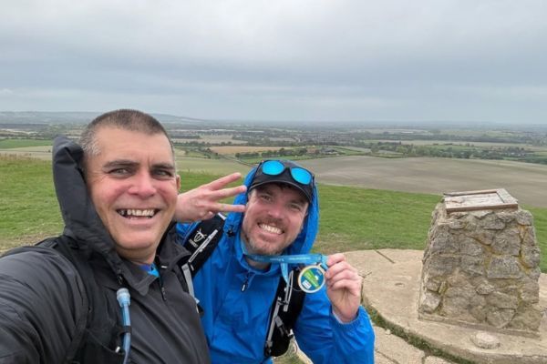 Derek and a friend holding up their medals on the top of a mountain.
