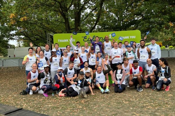 A group of runners wearing Meadow House branded vests smiling and waving.