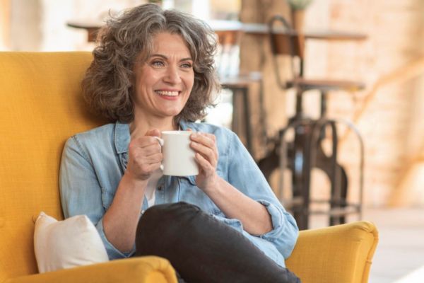 A lady sitting in a yellow chair with a cup of coffee.