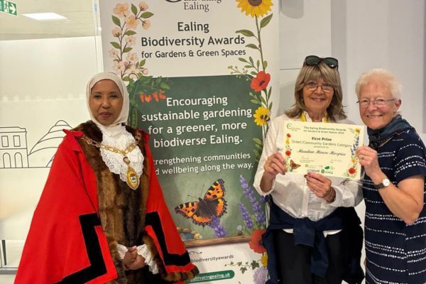 Gardening volunteers Carol and Ann, holding a certificate and the Mayor of Ealing Faduma Mohamed, standing next to a pull up banner with information about the Ealing biodiversity awards